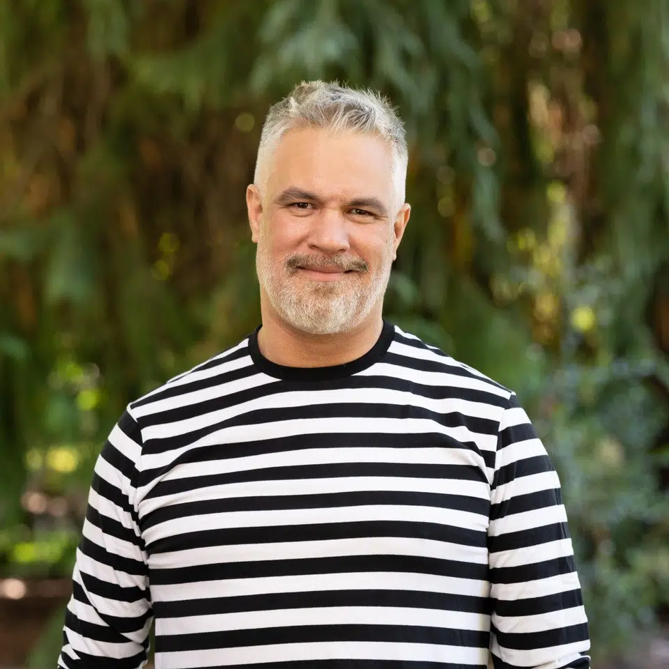 a smiling person with gray hair and a beard in a black and white striped shirt