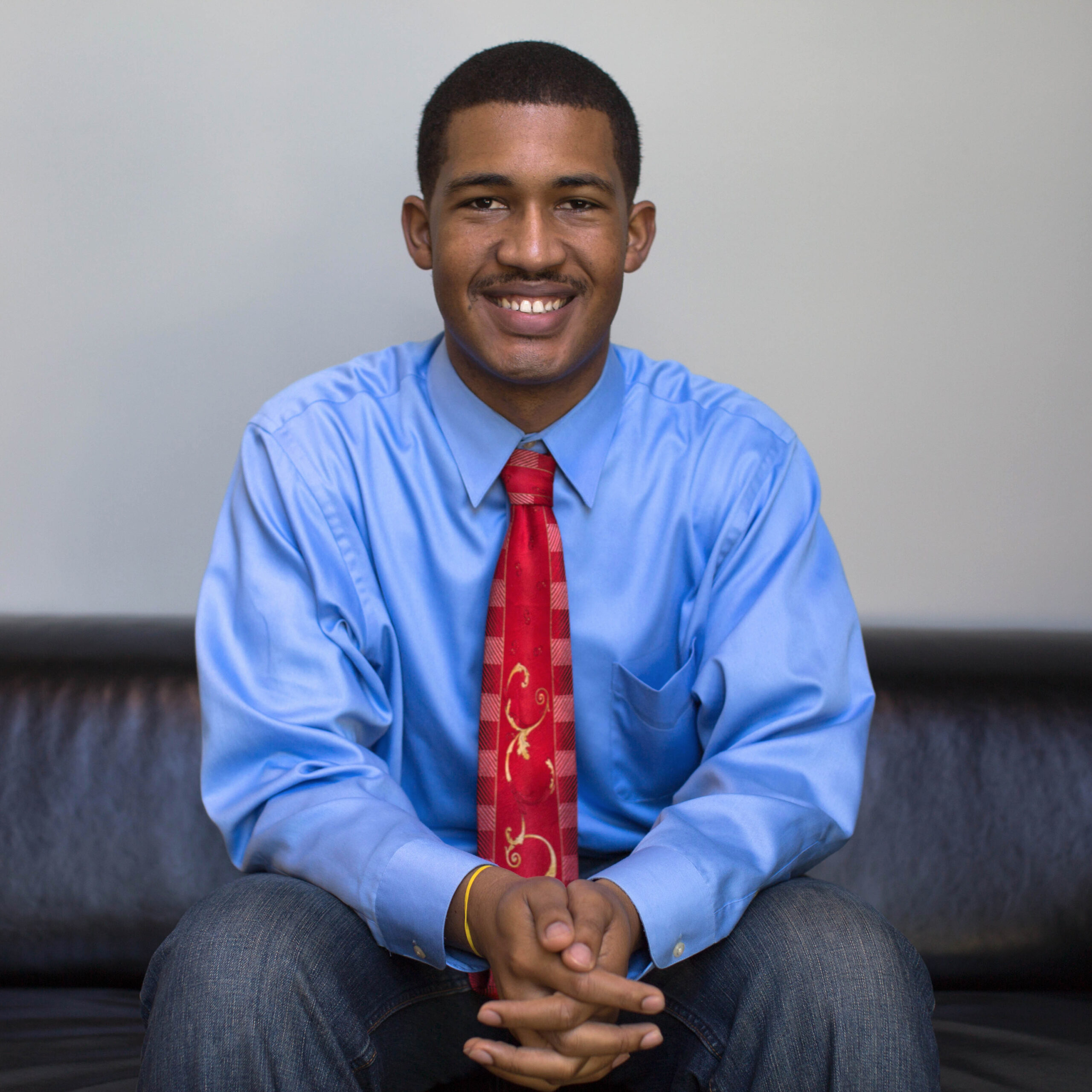 a smiling person in a blue shirt and red tie
